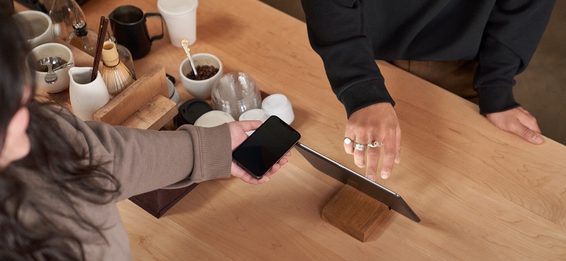 Kunde, der ein mobiles Gerät verwendet, um einen sicheren Einkauf im Kaffeehaus zu tätigen