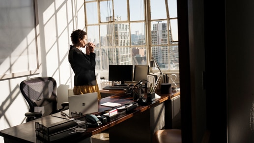 Woman drinking from a cup looking through an office window