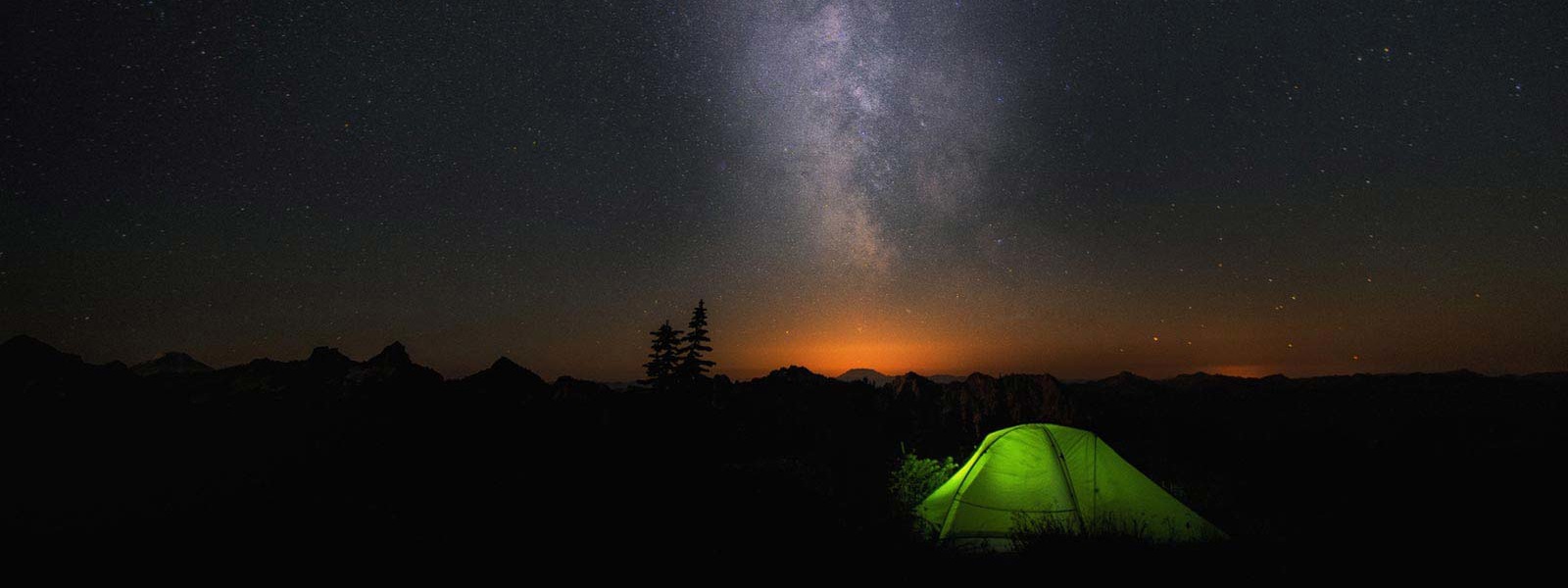 An illuminated tent sits under the milky way.