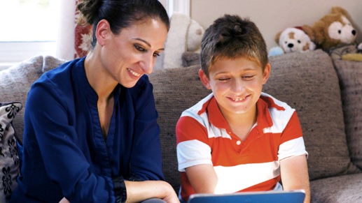 A mother and son smile as they look at a device together.