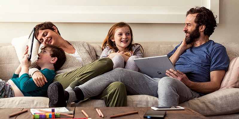 Family sitting together on the couch using a laptop and tablet.