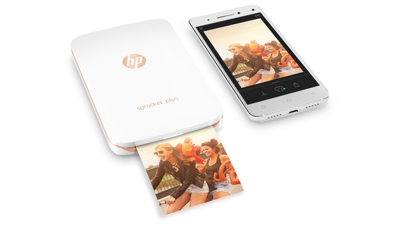 Birdseye view of the HP Sprocket in white while printing next to a smartphone