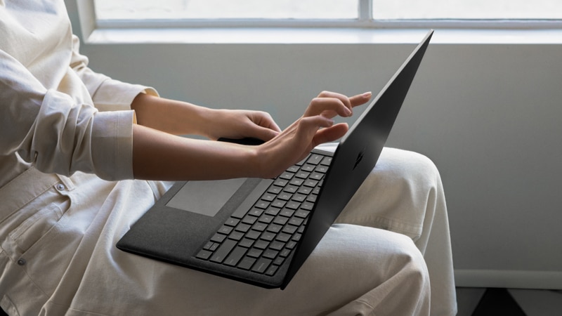 A person with Surface Laptop 2 on their lap uses touch navigation on the touchscreen laptop