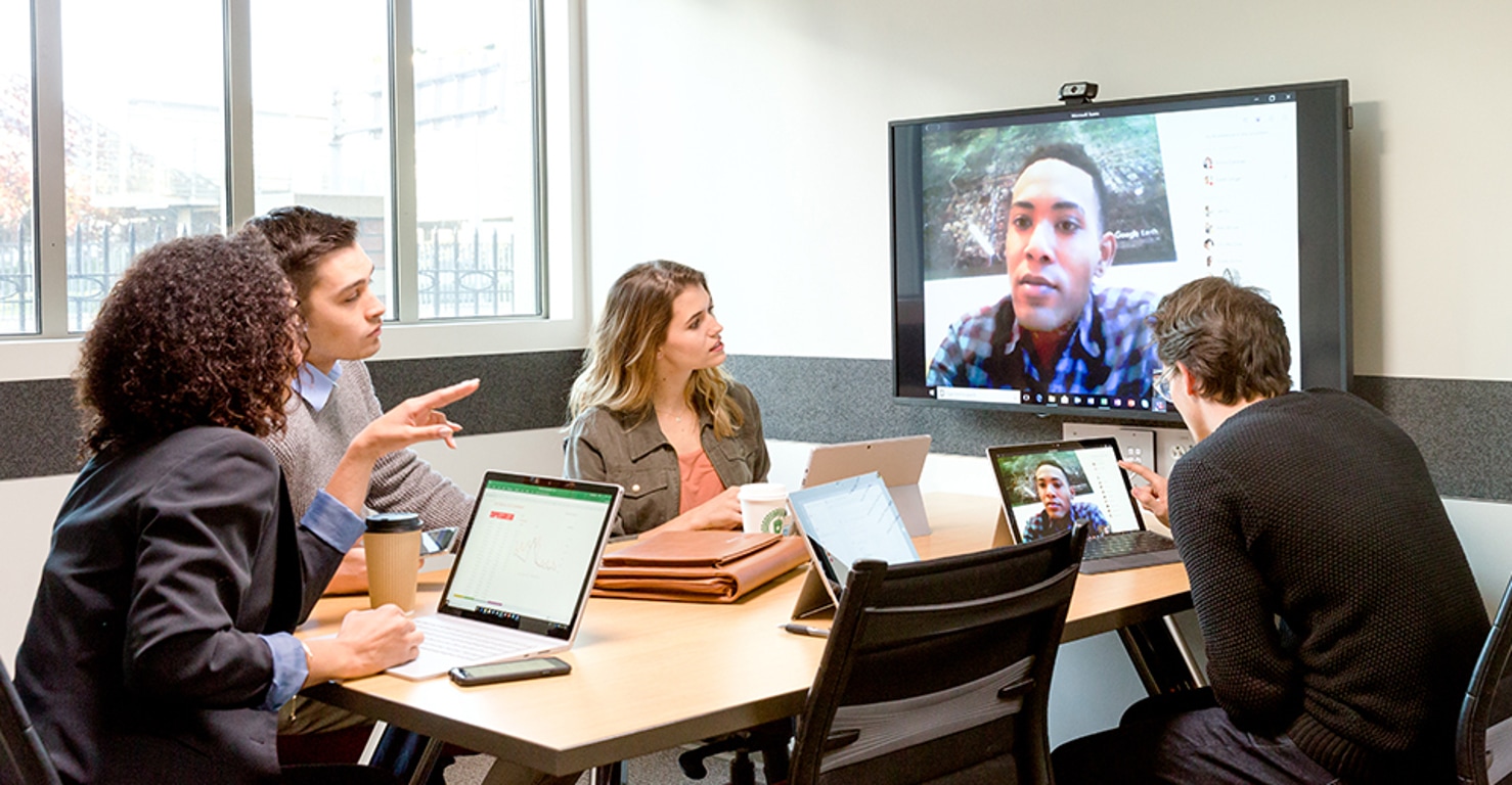 A group of co-workers video conferencing with a colleague in a conference room