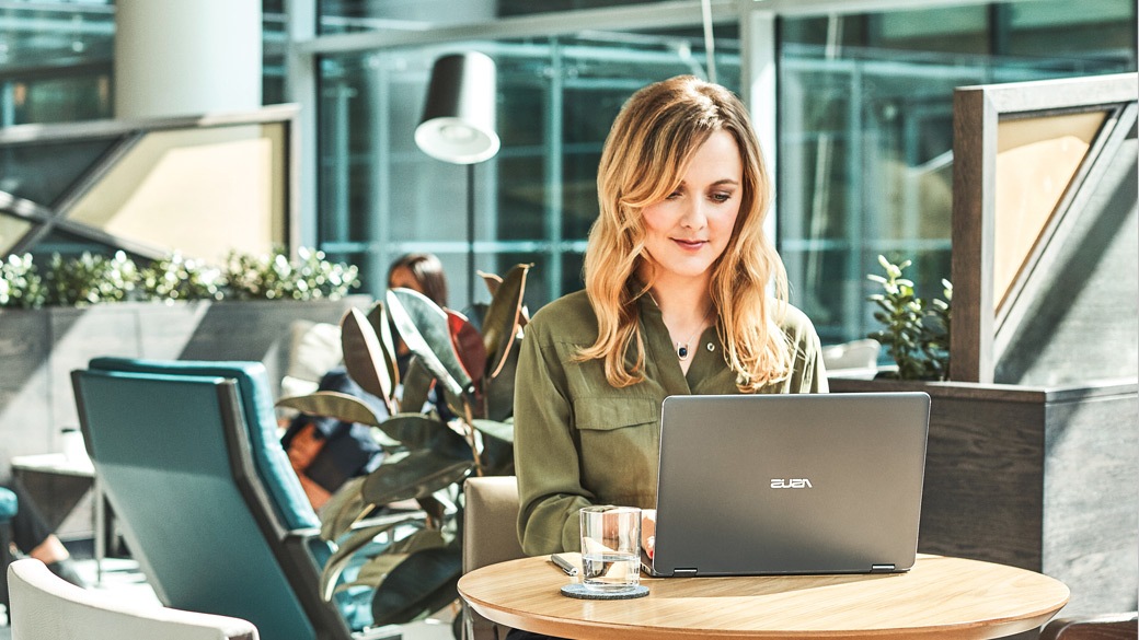 Mulher em uma mesa redonda no escritÃrio interagindo com seu PC com Windows 10.
