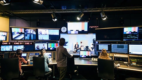 Broadcasting room three women sitting one standing looking from behind