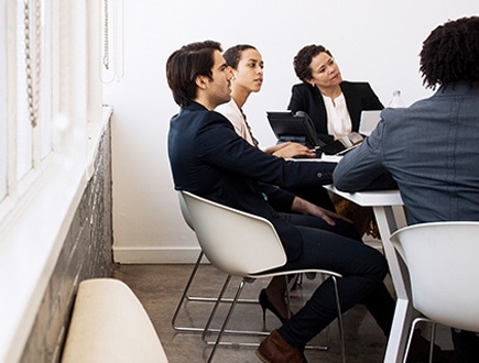 Photograph of four people sitting at a table in a conference room listening to someone who is out of frame