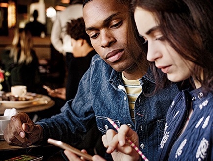 Photograph of two people sitting at a café table using a mobile device