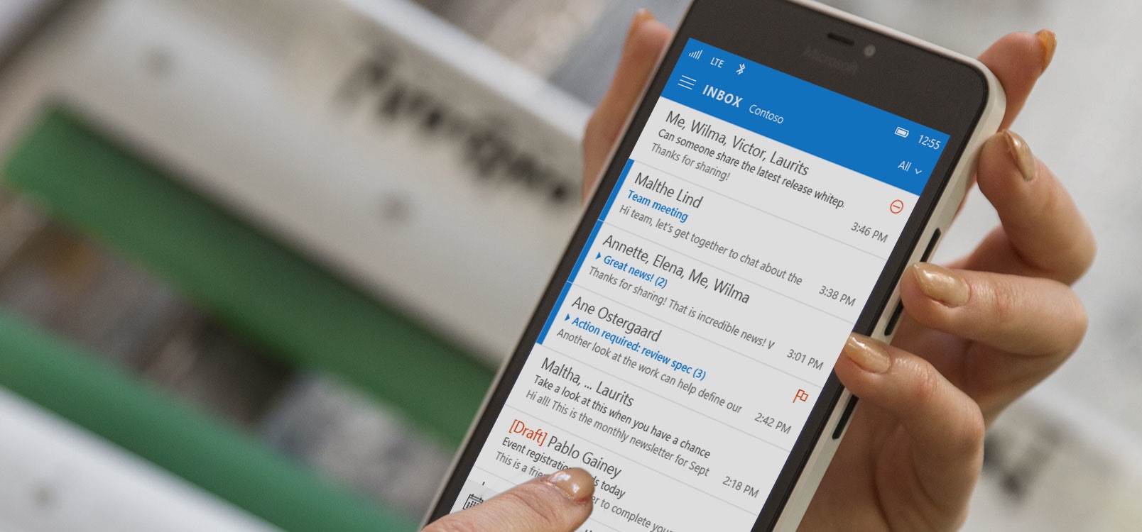 A hand tapping a message in an Office 365 email list on a smartphone.