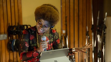 Singer/songwriter SassyBlack in studio holding microphone with Surface device