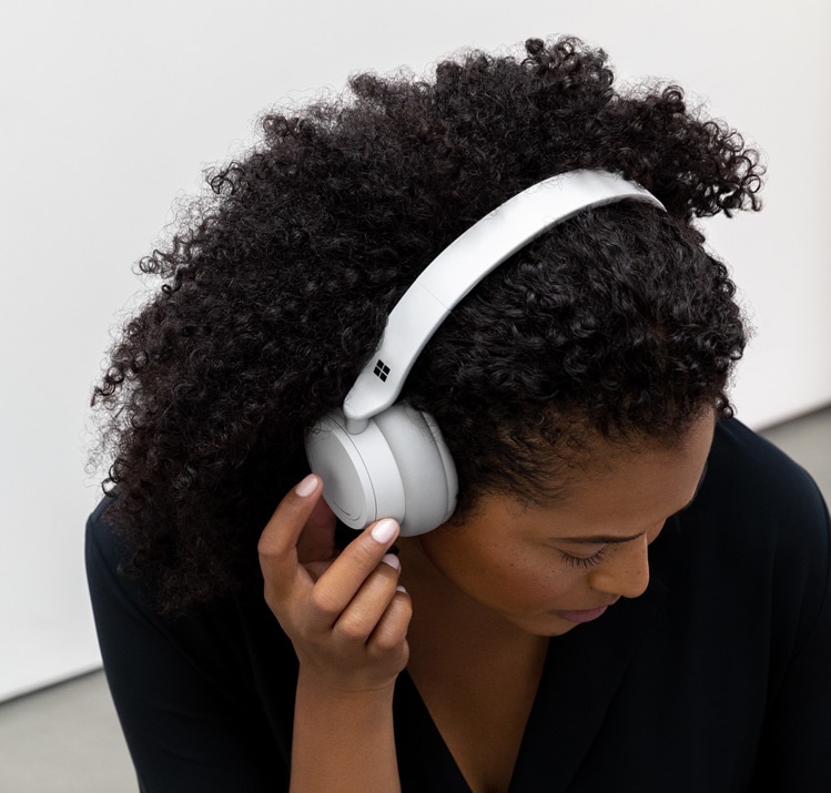 頭につけた Surface Headphones で音楽を聴いたり話したりする女性