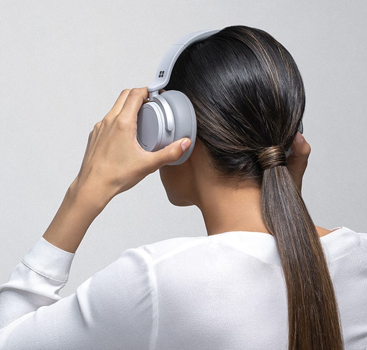 Eine Frau setzt sich Surface Headphones auf den Kopf