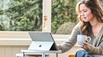 Person holding a coffee cup seated at a small table using a Surface Pro 6