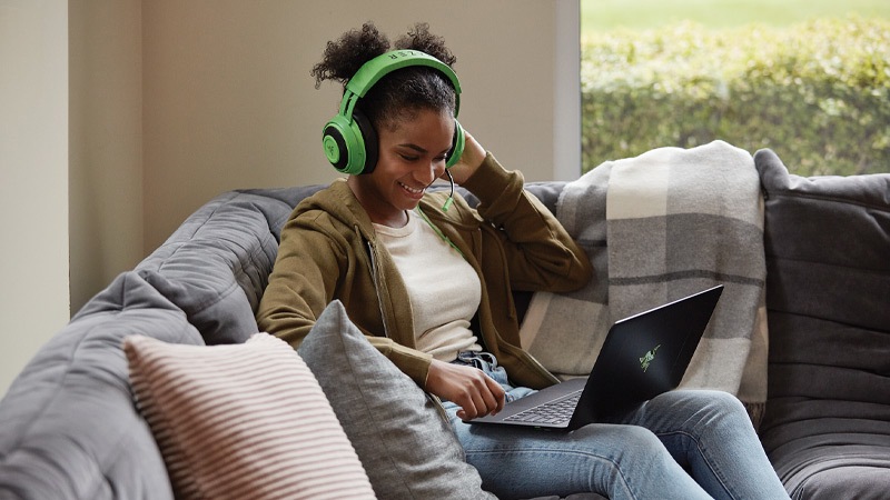 Una joven con auriculares disfruta un juego en su equipo con Windows 10 recostada en un sofá.