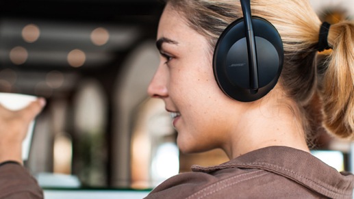 A woman is ordering a coffee while using her Bose NC Headphones 700 Black
