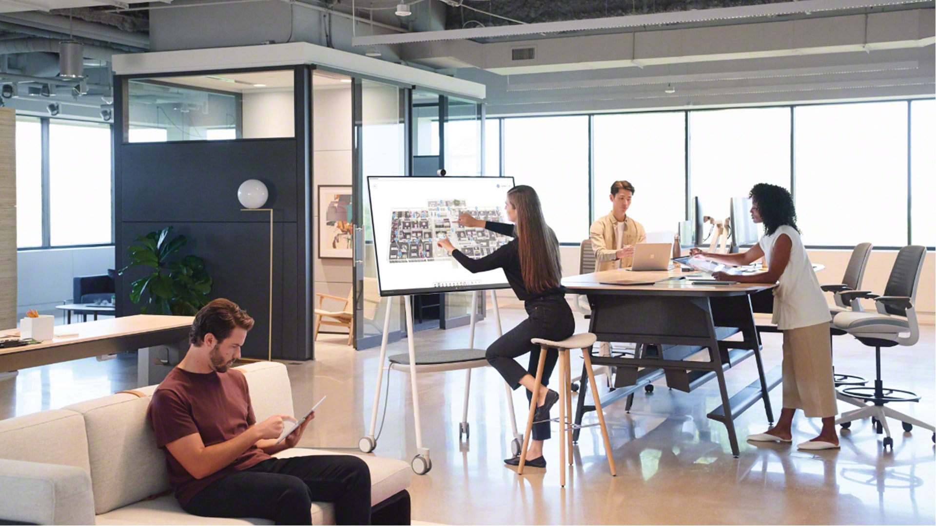 Großraumbüro, in dem ein Team arbeitet. Frau mit Surface Hub 2S in der Mitte des Fotos