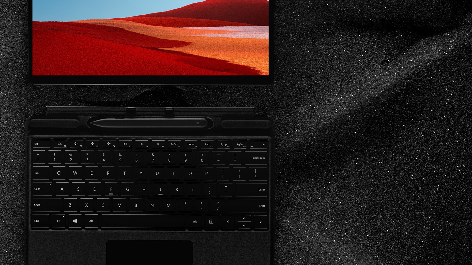 Surface Pro X with Surface Slim Pen and Surface Pro X Signature keyboard laying flat on black sand