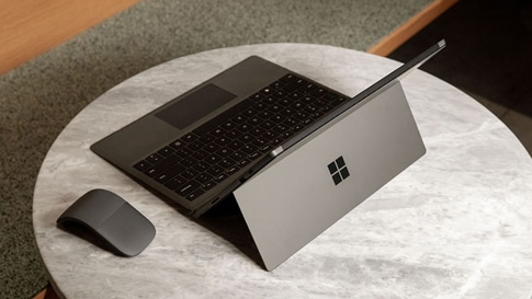 Ordinateur portable tactile Surface Pro 7 en noir mat avec la souris Surface Arc Mouse sur une petite table