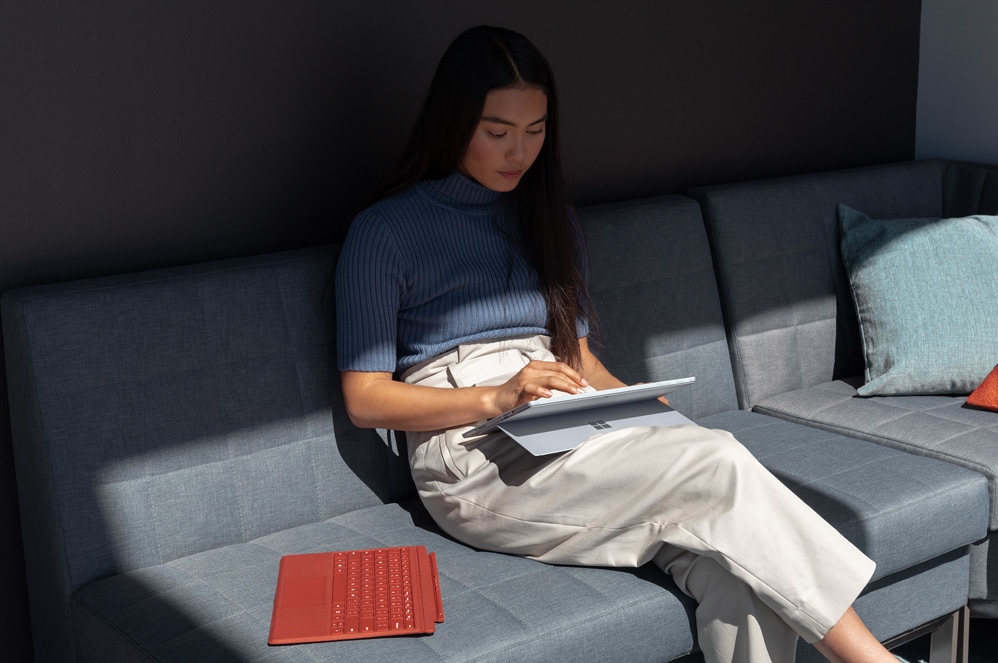 Une femme travaille sur un canapé, un ordinateur portable tactile Surface Pro 7  sur ses genoux.