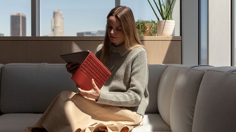 一位女性坐在沙发上打开附有罂粟红键盘盖的 Surface Pro 7