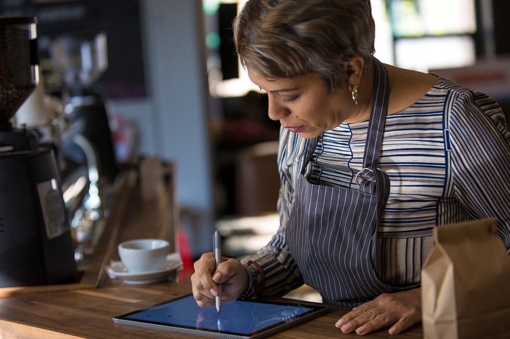 A woman who works in a café writes on Surface Pro with Surface Pen