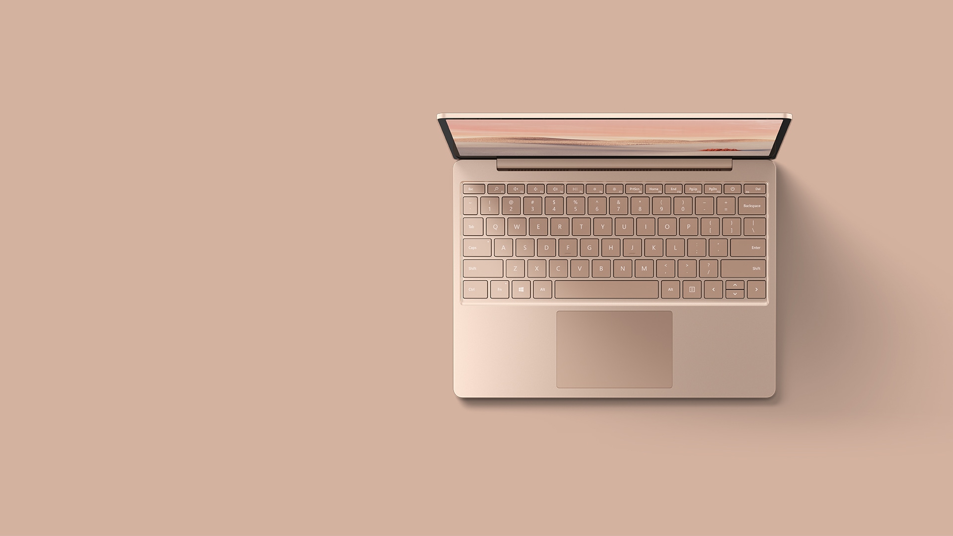 An aerial view of the sandstone Surface Laptop Go resting upon a matching background.