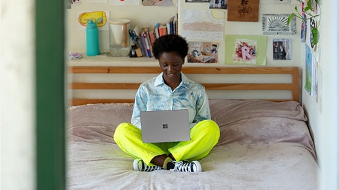Person sitting on a bed typing on Surface Laptop Go