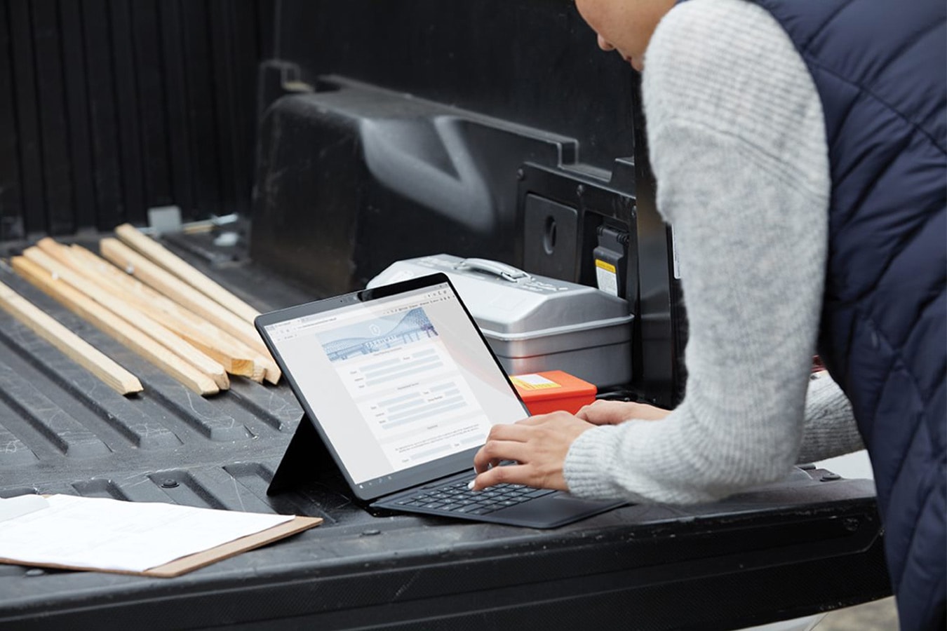 Eine Person arbeitet mit ihrem einem Surface Pro X vom Rücksitz ihres Pickups aus