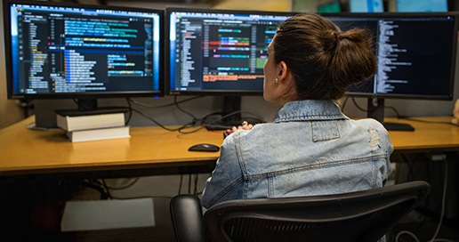  Person sitting looking at code displayed on three large desktop monitors.