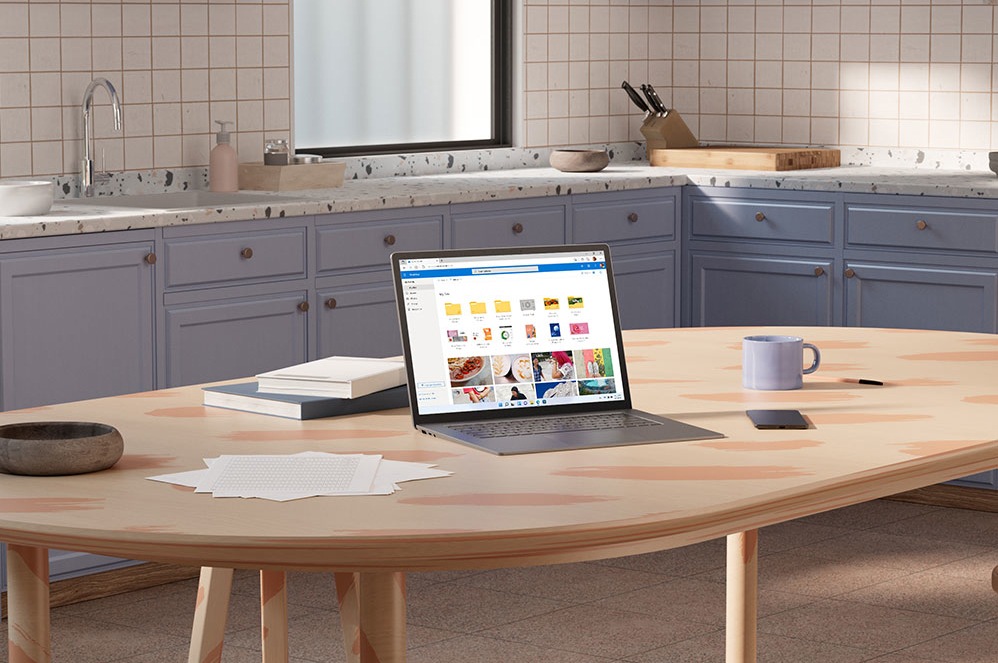 En tablet, der viser Microsoft OneDrive, ved siden af en notesblok, en lampe og en skål med papirclips.