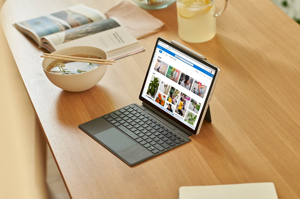 Tablet yang menampilkan Microsoft Word berada di samping tanaman, botol air, dan kartu identitas.