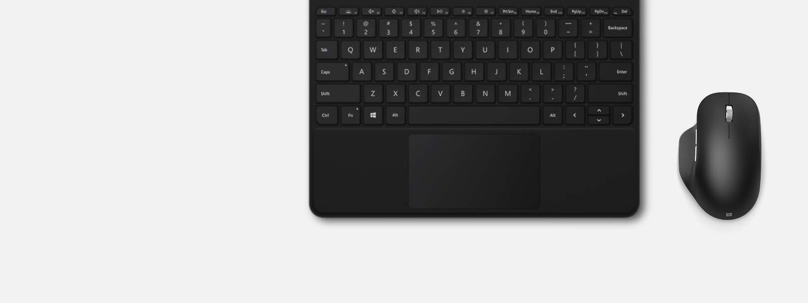 Um Microsoft Bluetooth Ergonomic Mouse em Preto fosco em uma mesa ao lado de um teclado numérico