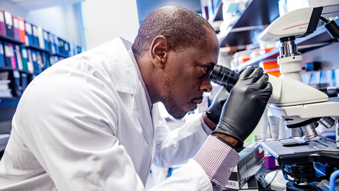 Um cientista com jaleco branco olhando em um microscópio.