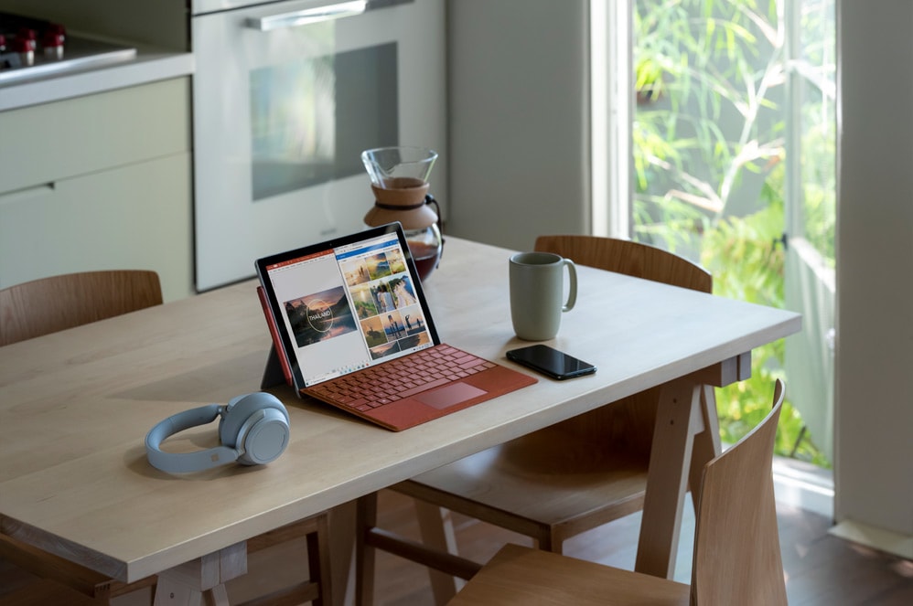 Komputer Surface Pro 7 znajdujący się na stole obok słuchawek Surface Headphones 2 i telefonu komórkowego