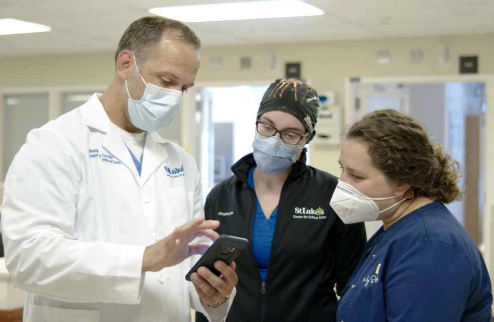 Three medical professionals wearing PPE looking at a mobile device.