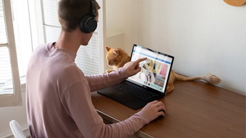 Person using Surface Laptop 3 PixelSense™ Touchscreen and Surface Mouse while wearing Surface Headphones 2