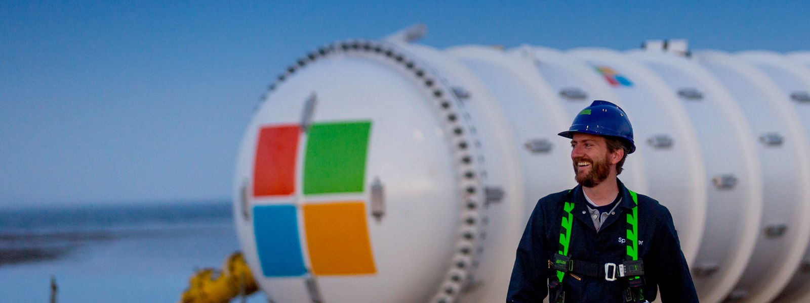 Microsoft 로고가 새겨진 가스 탱크 앞을 걸어가며 미소 짓는 산업 노동자