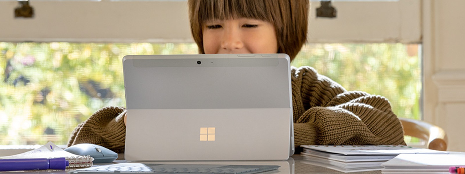 Ребенок, работающий на Surface Go 2 дома с крышкой типа Ice Blue Surface и ручкой Surface