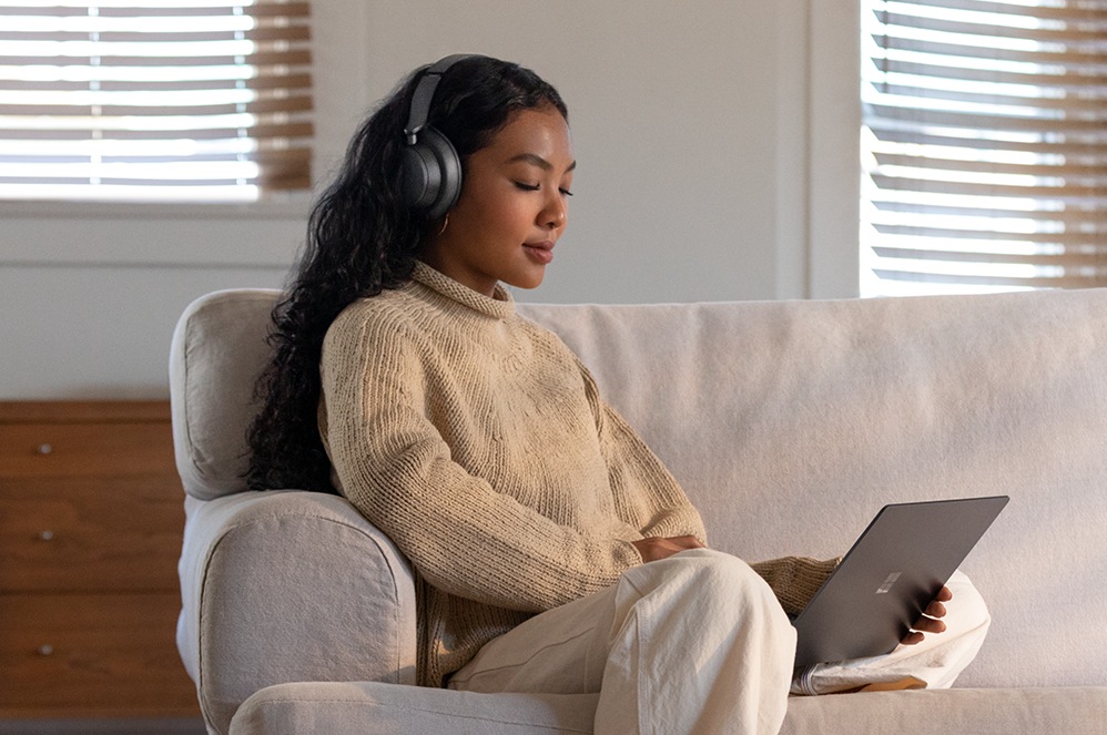 Person wearing Surface Headphones+ and holding a Surface device.