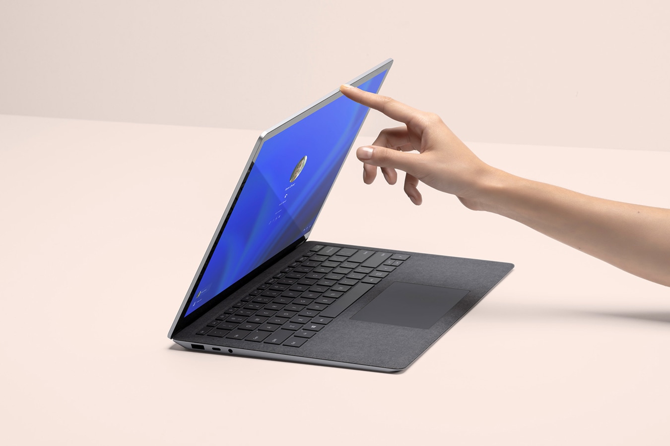 A person’s hand is shown lifting the lid of a Surface Laptop 4, with the sign on screen shown