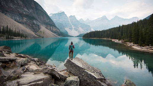 Una vista panorámica con una persona frente a un paisaje de montaña y un lago azul cristalino