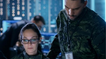 Two military personnel in uniform looking at a device together.