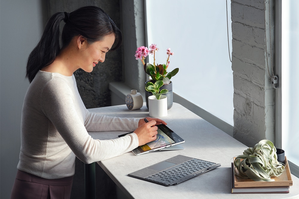 Une personne assise à un bureau, travaillant avec le stylet Surface Slim Pen 2 et le clavier Signature Keyboard pour Surface Pro.