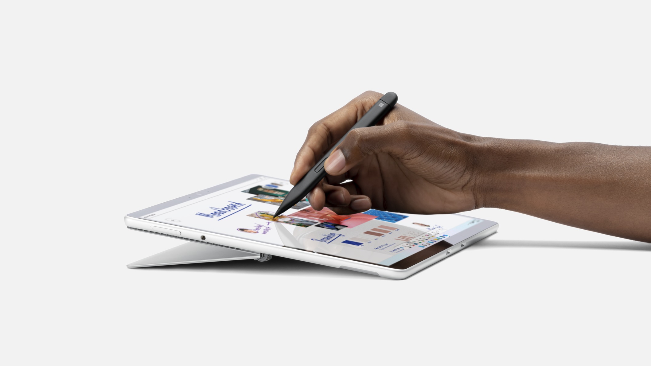 A person’s hand holding Surface Slim Pen 2 and writing on a Surface device screen.