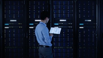 A person standing in a server room looking at a tablet device.