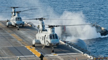 Two military helicopters on an aircraft carrier in the ocean.