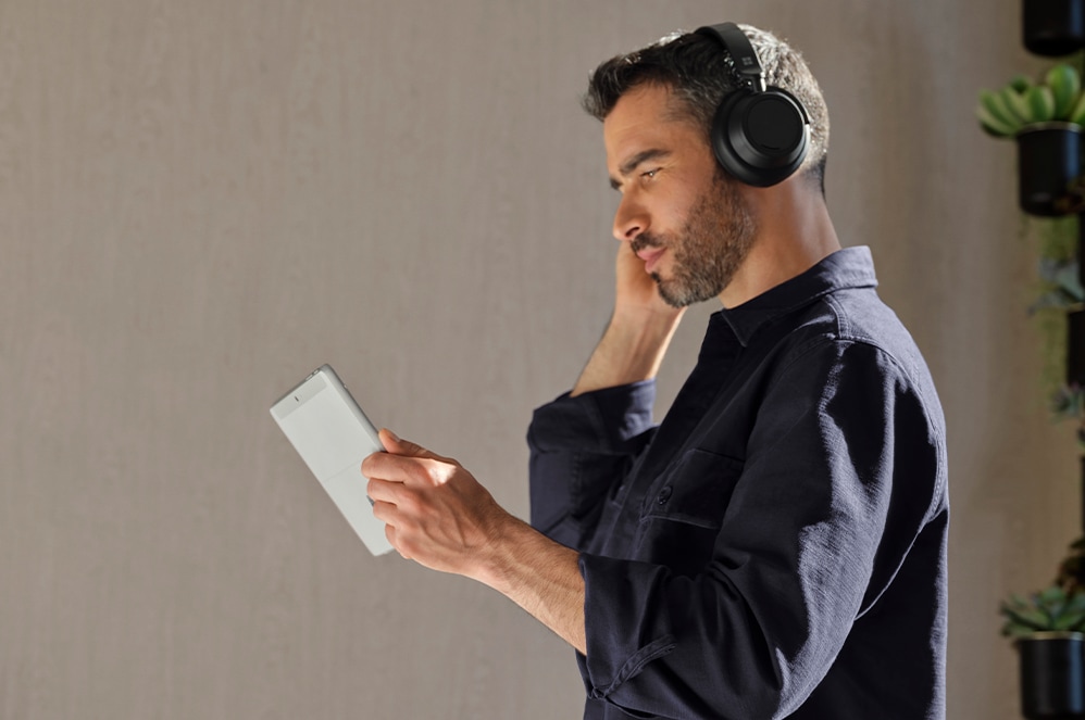 Henkilö pitää kiinni Surface Go 3 yrityksille -laitteesta ja käyttää Surface Headphones -kuulokkeita.