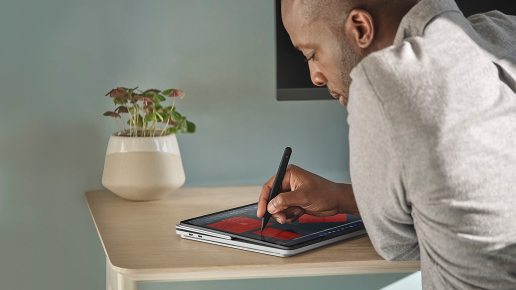 A person's hand removing Surface Slim Pen 2 for Business from the cover of Surface Laptop Studio for Business.