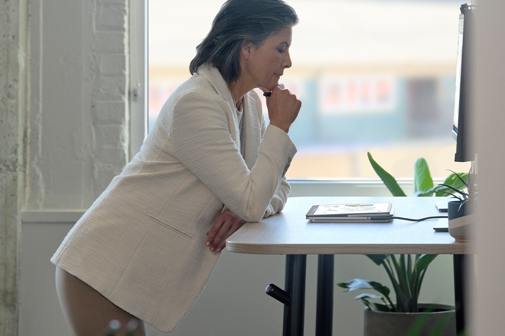Eine Person steht an einem Schreibtisch und schaut auf Surface Laptop Studio for Business.