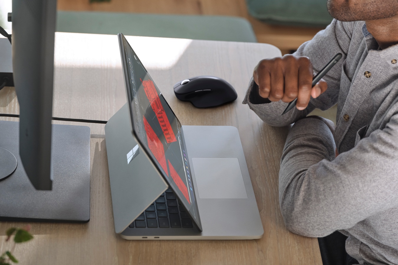 A person sitting at a desk holding Surface Slim Pen 2 for Business, working with Surface Laptop Studio for Business.